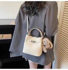Detailed view of white pebble leather bucket bag with silver clasp and plush rabbit charm