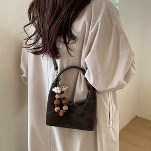 Detail of dark brown suede dumpling bag with contrast stitching and plush ball charm