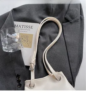 Detail of creamy white bucket bag featuring adjustable straps and metal eyelet accents