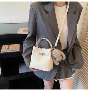 Detail of creamy white lychee grain leather bucket bag with silver twist lock and charm