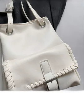 Detail of woven stitching and metal buckle on white leather shoulder bag with smooth texture