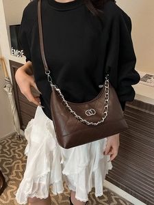 Sac bandoulière matelassé marron avec logo double anneau argenté porté par un mannequin