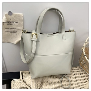 Close-up of light gray tote bag with visible stitching and adjustable strap on a chair