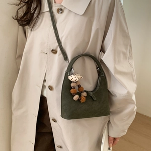 Detail of dark green crescent bag with decorative bow and beads on beige trench coat