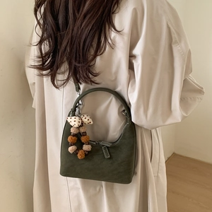 Detail shot of green dumpling shoulder bag with white stitching and plush charms on a coat