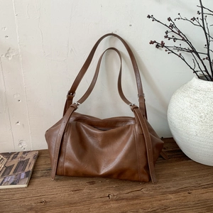 Detail of caramel brown leather tote bag with adjustable buckle straps on a wooden surface