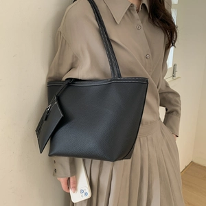 Detailed view of black leather tote bag with white stitching and detachable pouch on model