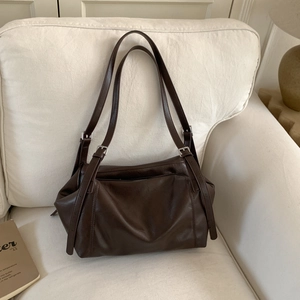 Detailed view of the dark brown retro tote bag with silver buckles on a soft white sofa