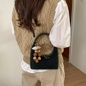 Detail of black suede dumpling bag with white stitching and bead tassel on model