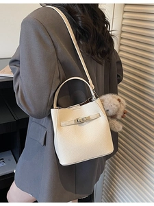 Beige lychee leather bucket bag with metal turn-lock and plush charm on female model