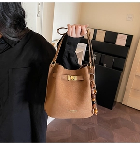 Détail du sac seau en daim marron avec fermoir doré et pendentif en perles de bois