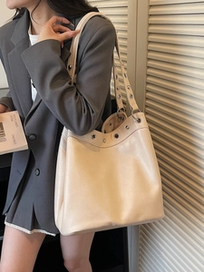 Minimalist beige tote bag with silver metal eyelets shown on a model in a grey suit