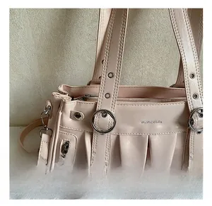 Detail of pink leather tote bag featuring a round metal buckle and fringed zipper accents