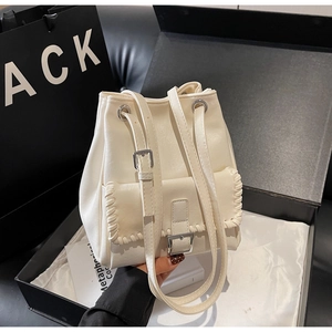 Détail du sac seau crème avec bords tressés et boucle argentée dans une boîte cadeau