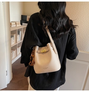 Détail du sac seau crème avec fermoir rotatif doré et pendentif en perles de bois