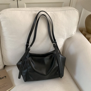 Detail of minimalist black PU leather tote bag with pleated texture on white sofa