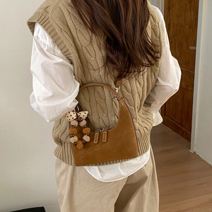 Brown suede hobo bag with colorful pom-pom charm worn over a beige knitted vest