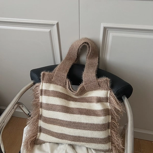 Détail du sac cabas en maille rayée avec de longues franges sur une chaise en cuir