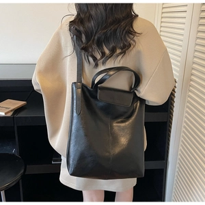 Détail du sac cabas en cuir noir avec rabat texturé et bandoulière élégante sur le modèle