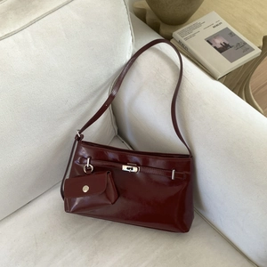 Sac sous le bras en cuir verni bordeaux avec fermoir argenté sur un canapé