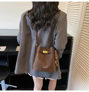 Détail du sac seau en daim marron avec fermoir rotatif doré et pompon en perles