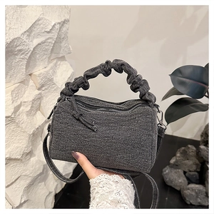 Detail of grey textured denim crossbody bag with ruched handle and dual metal zippers