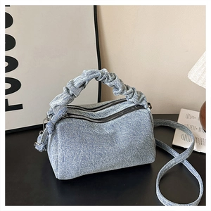 Detail of light blue denim Boston bag featuring ruffled handles and dual zipper closure