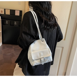 Close-up of white bucket bag featuring elegant whipstitch trim and decorative metal buckle