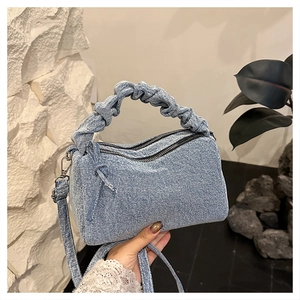 Detail of light blue denim cylinder bag featuring pleated handle and double zipper closure