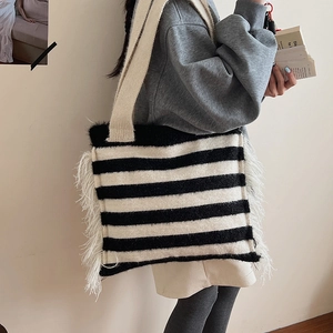 Détail du sac cabas en maille rayée avec de longues franges blanches porté à l'épaule