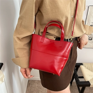 Red glossy leather tote bag with dual handles and detachable shoulder strap on model