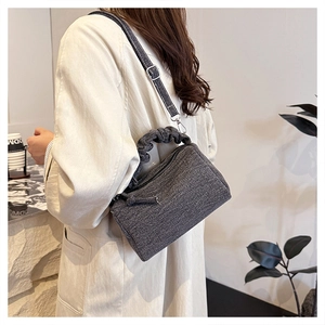 Detail of ruched handle and denim texture on grey crossbody bag with metal zipper