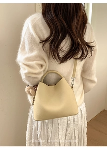 Detail of beige textured leather bucket bag with cute bear charm worn by a model