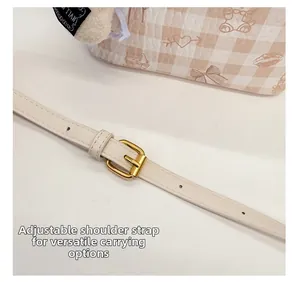 Detail of adjustable leather strap with gold buckle on plaid patterned shoulder bag