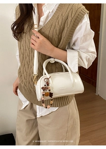 White minimalist Boston bag with handle and beaded charm shown on model in a bright room