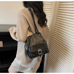 Close-up of black bucket bag featuring woven edge details and a large metal square buckle