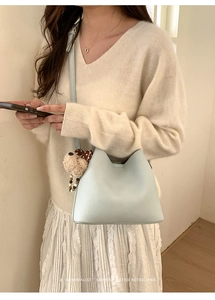 Detail of light blue bucket bag with cute brown plush dog charm on a beige outfit