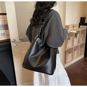Detailed view of black leather tote bag with silver grommets worn by a model