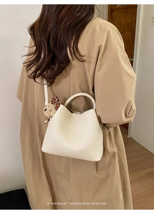 Detail of cream bucket bag with lychee texture and cute bear charm worn by a model