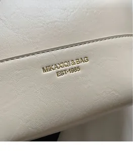 Close-up of minimalist brand logo and textured cream leather on a stylish handbag