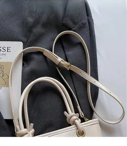Detail of cream leather bucket bag with woven handle and gold hardware on grey blazer