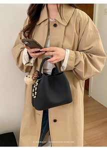 Minimalist black bucket bag with plush dog charm worn with a classic khaki trench coat