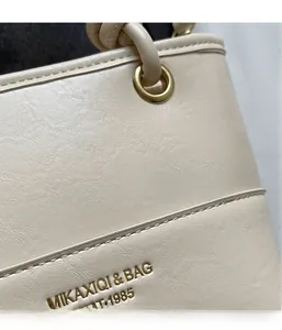 Close-up of beige leather tote bag with gold logo and premium stitched grain texture