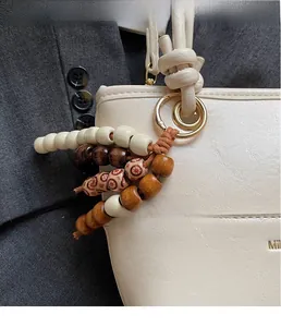 Detail of beaded bag charm with wooden beads and gold ring on a cream leather handle