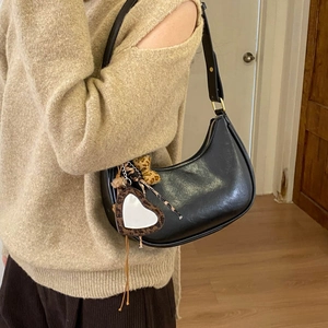 Détail d'un sac hobo croissant en cuir noir avec miroir cœur et accessoires léopard