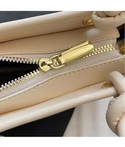 Detail view of the shiny gold metal zipper pull on a cream textured leather handbag