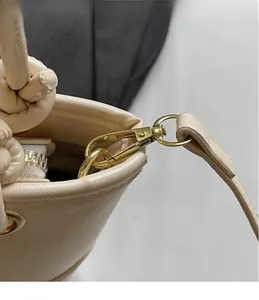 Detail view of light beige bucket bag showing gold hardware hooks and leather texture