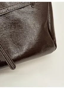 Macro detail of the dark brown glossy leather texture and neat stitching on the tote bag