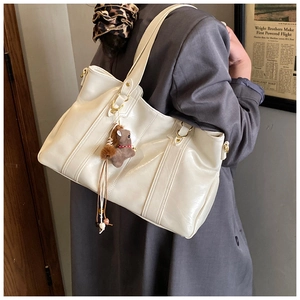 Dettaglio di una borsa in pelle bianco crema con ciondolo a cavallo e finiture dorate