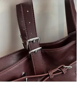 Gros plan sur la bandoulière réglable en cuir bordeaux avec boucle en argent poli du sac